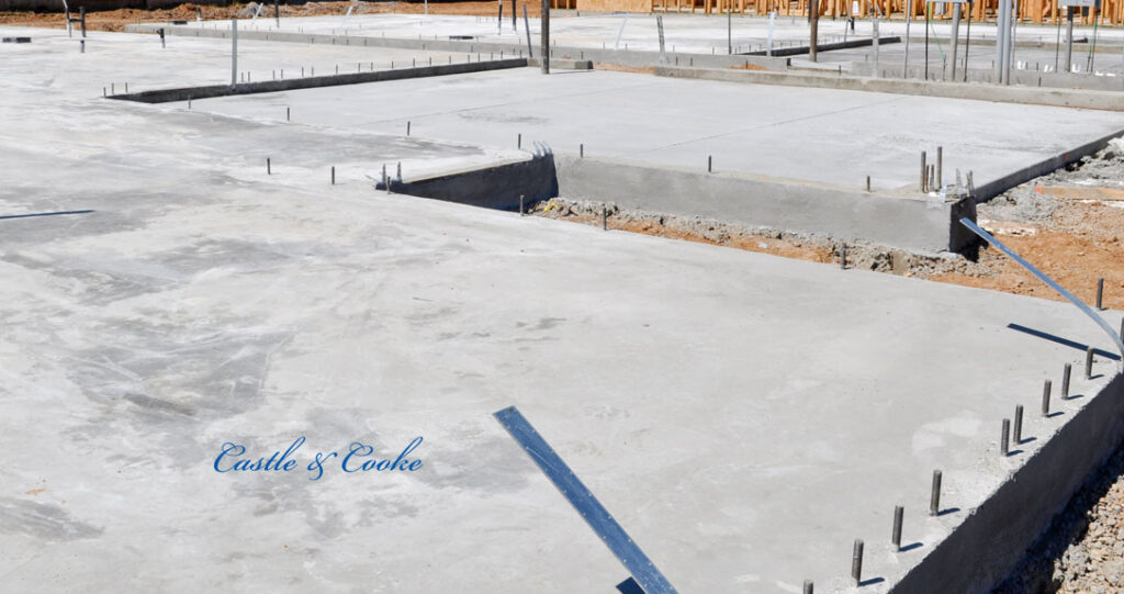Newly laid concrete foundations for a building, featuring exposed rebar and distinct sections of solid gray slabs, in a construction site setting.