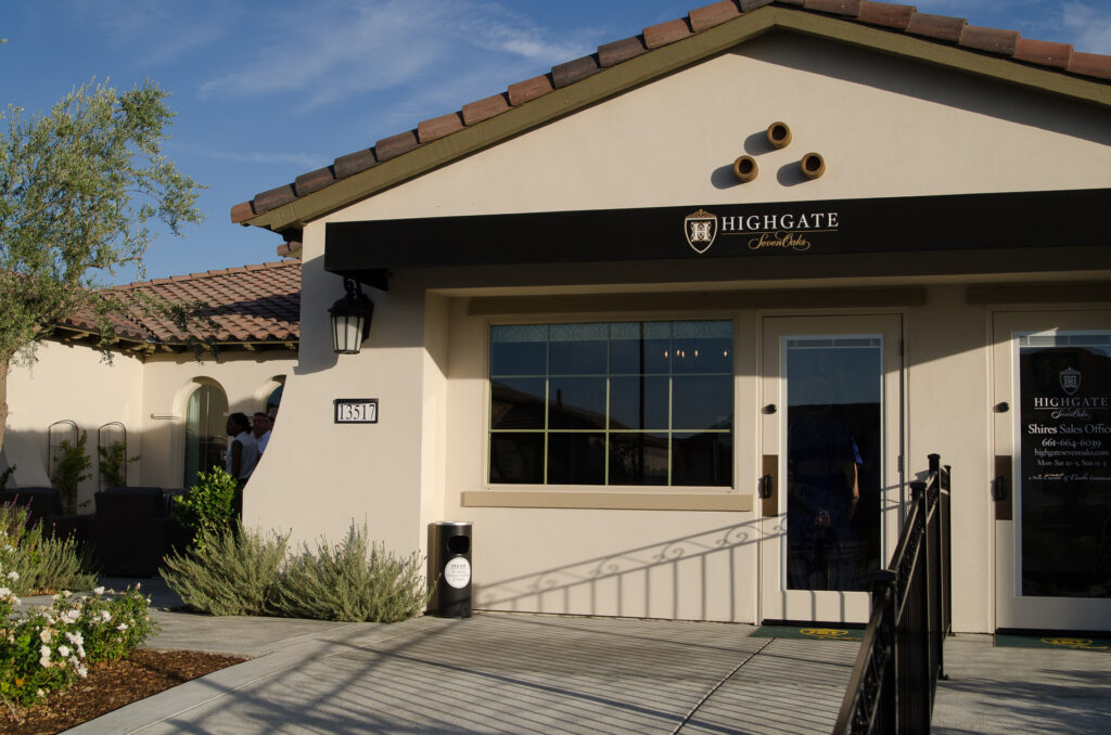 Exterior of the highgate senior living facility with a clear blue sky, featuring a beige building, terracotta roof tiles, and signage above the entrance. a ramp leads to the front door.
