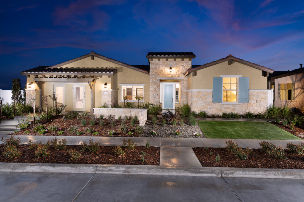 A large single-story house with stone accents, landscaped front yard, and dramatic evening sky. the house has a light exterior, a tile roof, and multiple windows.