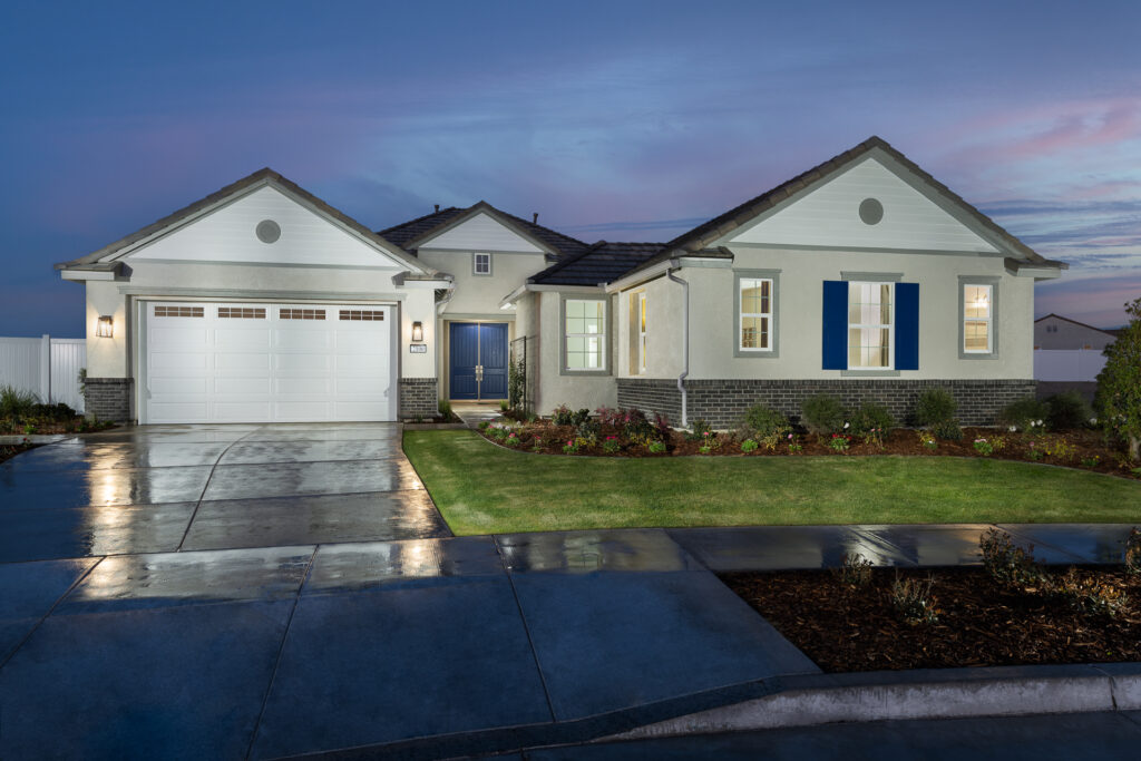 A modern single-story house at twilight with a landscaped front yard, driveway, and a two-car garage, featuring white walls and blue window shutters.