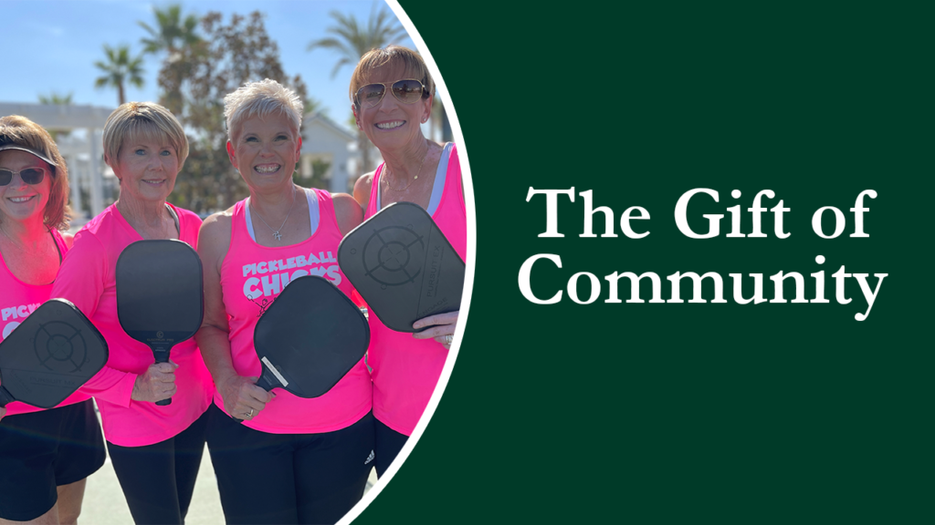 Four smiling women in matching pink tops and black pants, holding pickleball paddles, with text "the gift of community" on the right side against a teal background.
