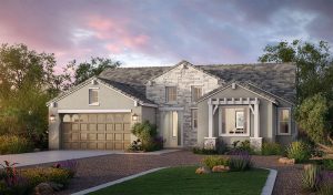 Modern single-story house with gray siding, stone accents, and a two-car garage. A front porch with white pergola, landscaped yard, and colorful flowers under a cloudy sunset sky.