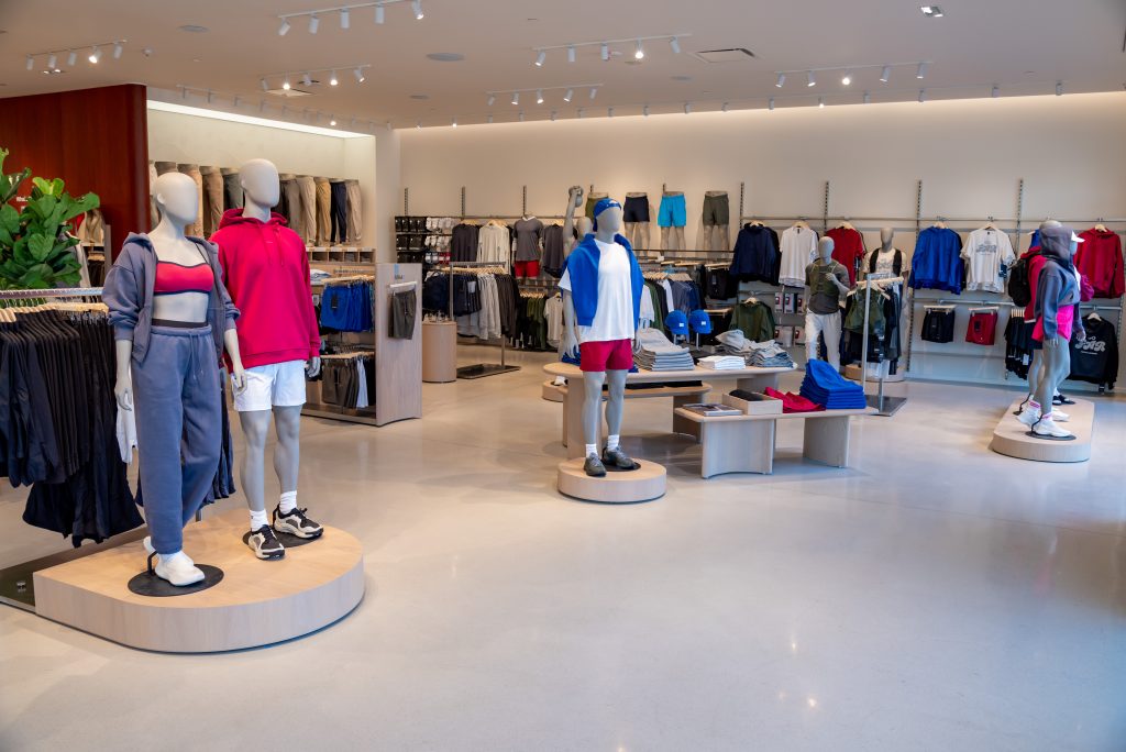 A modern clothing store interior with mannequins dressed in athletic wear, racks of clothes along the walls, and neatly arranged displays on circular platforms.