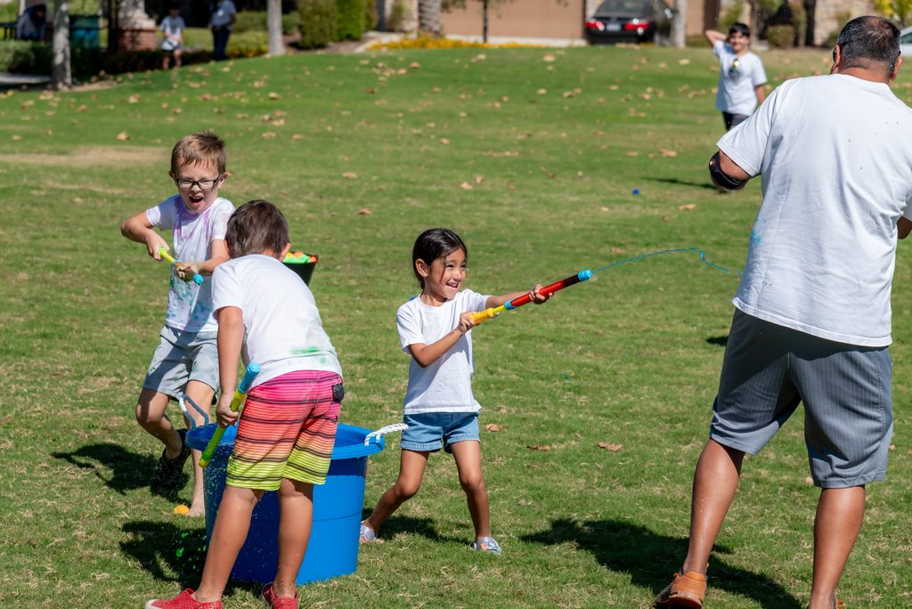 Children and an adult play with water shooters on a grassy field.