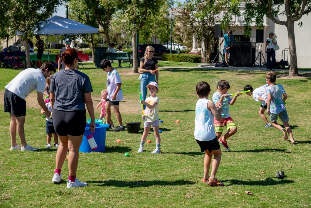 Children and adults play with water blasters in a grassy park.