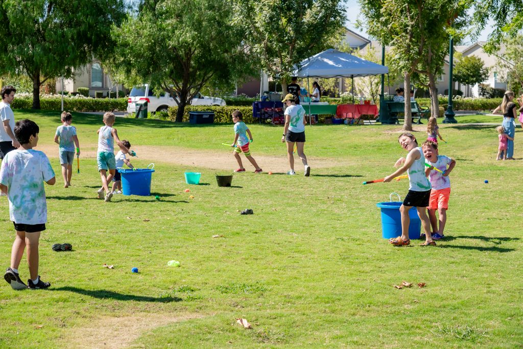 Children playing with water guns and buckets on a sunny park lawn.