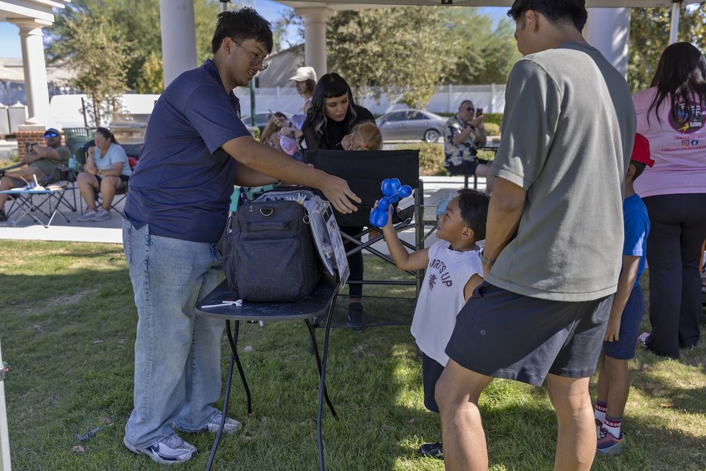 A man hands a blue balloon animal to a young boy at an outdoor event.