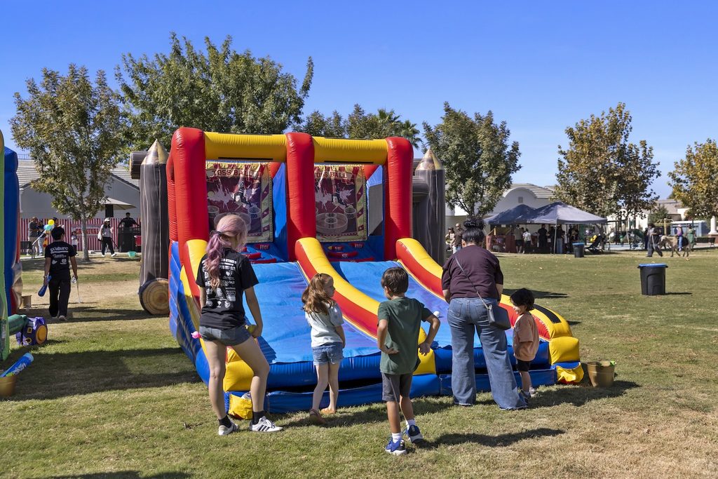 Children and adults play at a colorful inflatable toss game set up in a park.