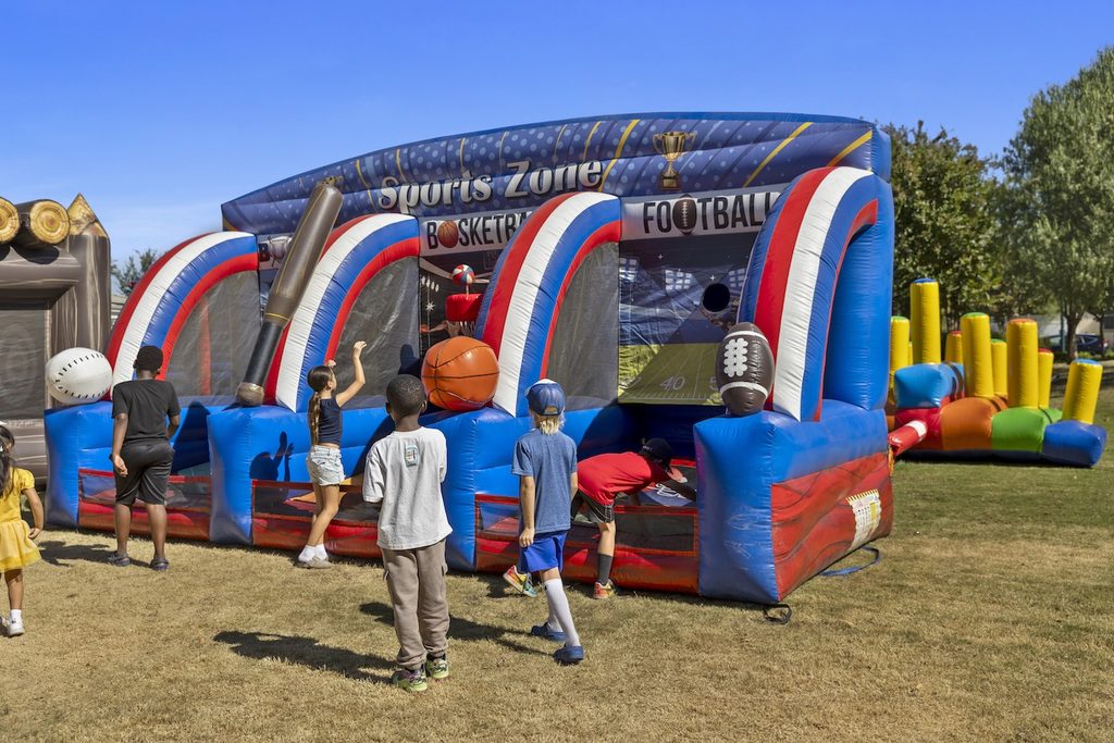 Children playing at an inflatable “Sports Zone” game station with basketball and football themes.